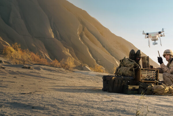 Soldier operating field communications equipment beside rugged cases and a military UAV drone in a mountainous environment.